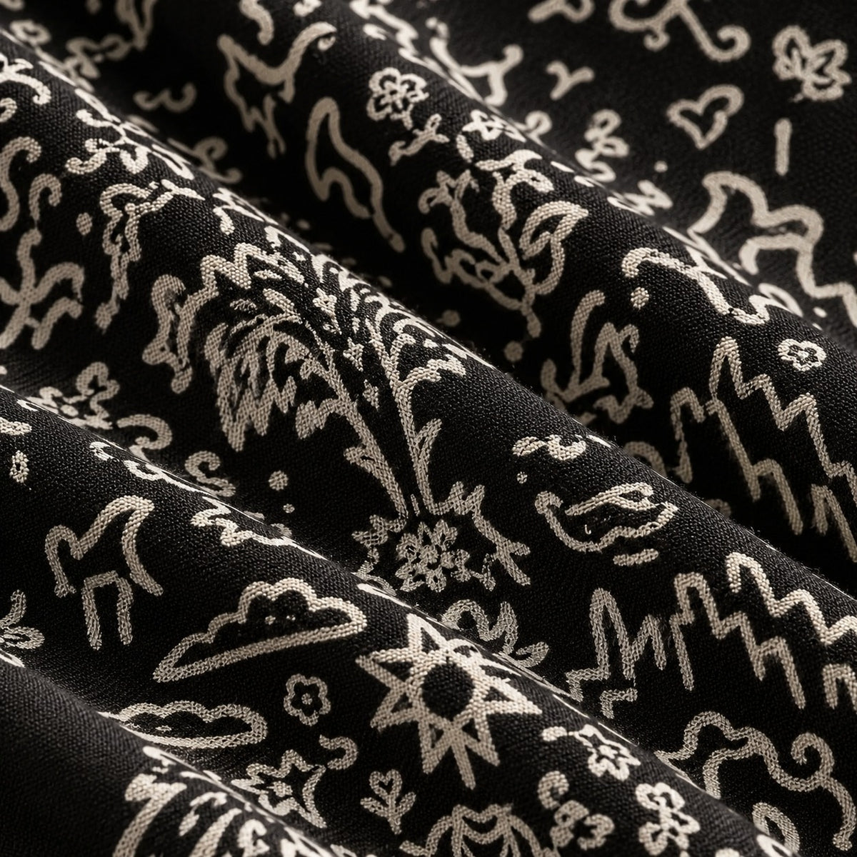 Close-up of the pattern: city skyline, horse, clouds and an eight-pointed sun in cream on black